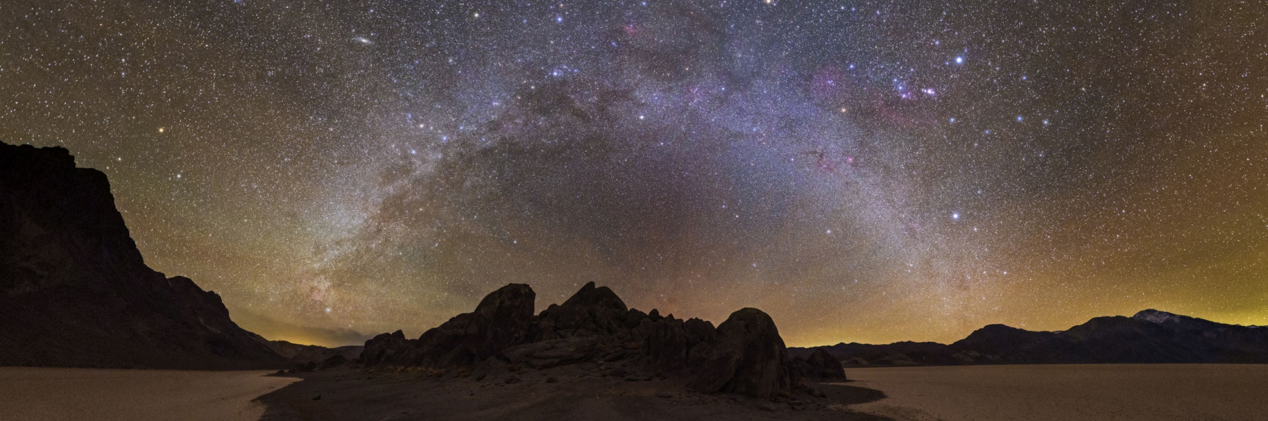 A photo highlighting stars in a twinkling Milky Way with rocky outcroppings below.