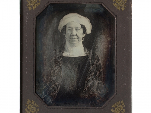 Black and white image of woman wearing dark dress and white headwrap in a small frame.