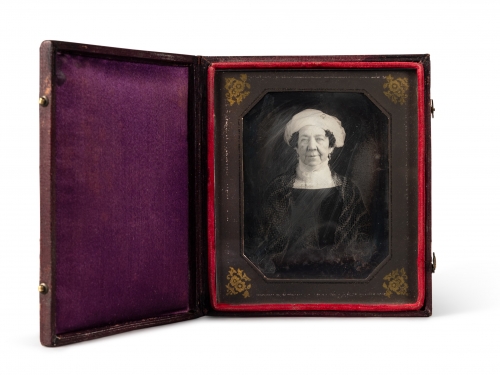 Black and white photograph of a woman wearing dark dress and white head wrap, in a small book-like frame.