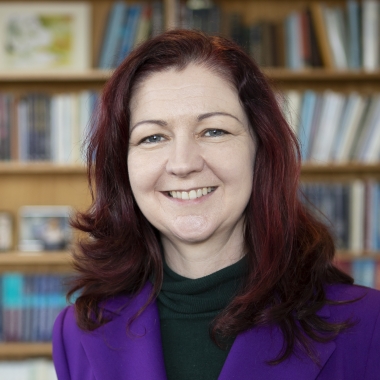 Lisa Kewley sits in front of a bookcase and smiles directly ahead