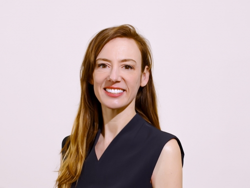 Woman with straight brown hair, wearing a black top, smiles toward camera.