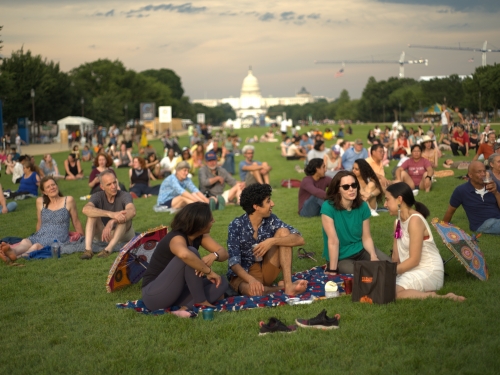 A group of four people sitting around chatting on a large patch of grass.